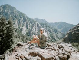 Girl traveling to mountains sitting on the edge of a cliff looking at trees on mountains