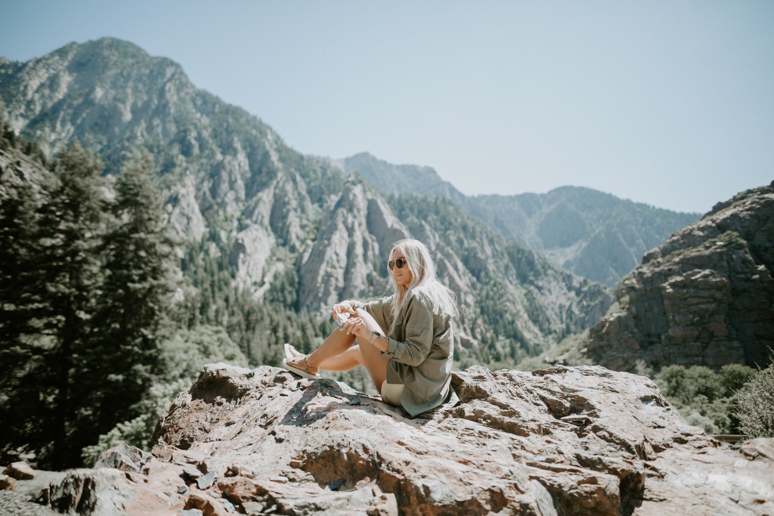 Girl traveling to mountains sitting on the edge of a cliff looking at trees on mountains