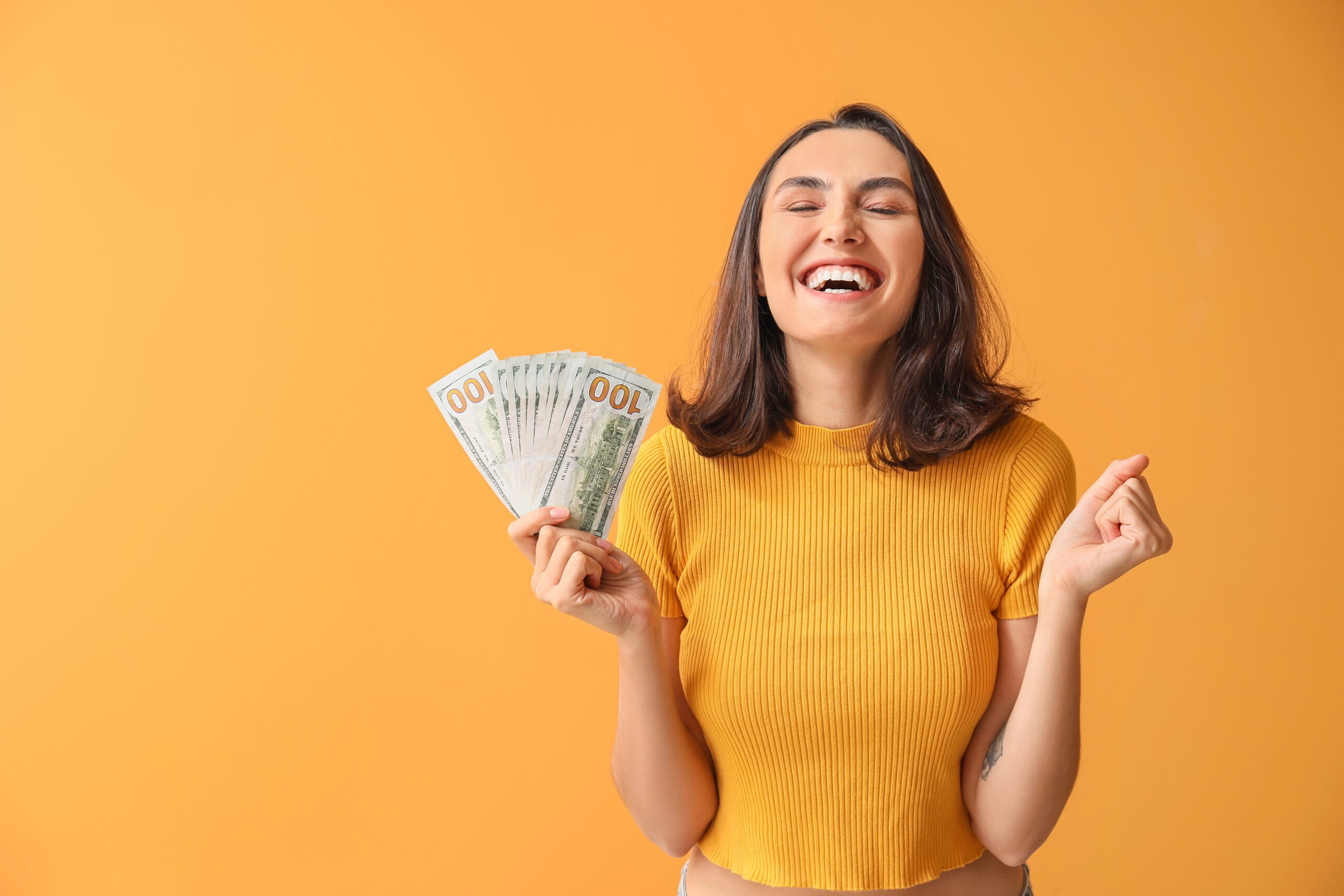 Woman smiling and holding cash in front of an orange wall