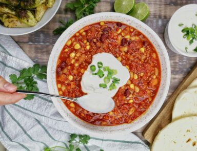 Image of chili in a bowl with sour cream being scooped on top