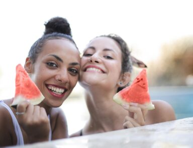 Two young women holding up slices of watermelon and smiling