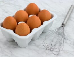 Eggs in carton next to whisk